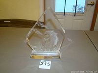 Clear glass pentagon-shaped decorative statue with etched lion and textured background, on solid glass base.