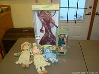Photo showing the boxed Victorian style porcelain doll, boxed Anne of Green Gables doll, and three fabric dolls on a table.
