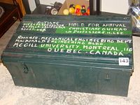 Front top view of green metal travel trunk showing hand-painted white and green lettering with addresses and names.