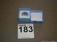 Ring displayed inside a small blue and purple gift box next to lid.