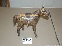 Front side of the small horse figurine showing leather saddle, bridle, and strap details on mottled brown body.