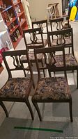 Six wood chairs with harp style backs, fabric upholstered seats with floral or abstract patterns, and curved legs shown in a group in a basement or storage area.