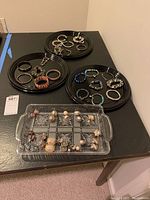 Overview of all costume jewelry items including bracelets on plates and earrings in divided glass tray on table