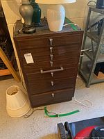 Front view of a seven-drawer wooden cabinet with metal handles and wear marks, surrounded by lamps and other items.