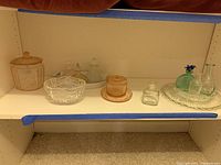 Shelf with collection of vintage glassware including pink glass jars, clear glass bowls, assorted glass cruets, and plates.