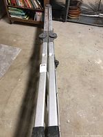Full length view of folded aluminum ladder showing two joined sections laid flat on the floor.