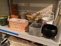 Shelf with various outdoor pots including terra-cotta, glazed ceramic, and painted ceramic planters.