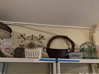 Photo showing the assortment of outdoor pots including metal pots, fabric basket, metal cage, wooden planter boxes, metal garden wall decor, and grapevine wreath arranged on a white metal shelf.