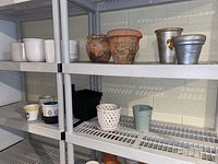 Shelf with assorted outdoor plant pots made of ceramic, terra cotta, and plastic showing full lot overview.