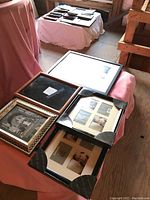 Assortment of picture frames in various styles and sizes arranged on a pink cloth-covered surface with more frames in background.