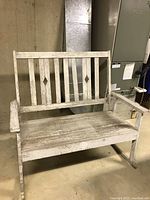 Front view of weathered wooden porch rocker bench showing diamond cutouts on backrest, armrests, and rocking base.