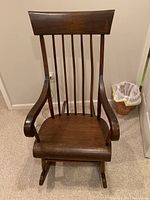 Front view of wooden rocking chair showing vertical slat backrest and curved armrests