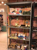 View of the gray metal shelving unit with various workshop storage items on shelves, showing sturdy metal construction and wear.