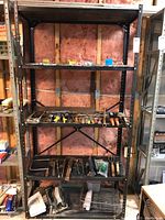 Front view of one black metal shelving unit showing weathering and contents on shelves (contents not included in sale)