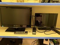 Both televisions are shown side by side on a shelf along with their respective remotes. The Element 19" TV is on the left and the Supersonic 13" TV is on the right.