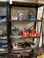 Shelf with various tools and hardware supplies including rope, measuring cup, pipe sections, and a red crate containing adhesives and small items.