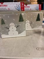 Close-up of two glass bricks showing snowmen, pine trees, snow, and falling snowflakes design with two packs of 20 indoor LED lights sitting behind them.