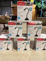 6 boxed Sunbeam Flexible LED Desk Lamps stacked in two rows, showing full product boxes with lamp image and branding.