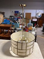Full view of the chandelier showing hanging rod, canopy, and cylindrical shade with brass frame on a table.