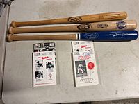 Lot showing three baseball bats aligned and four baseball programs laid out beneath them on a floor.