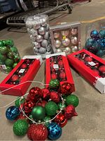 Multiple sets of Christmas ornaments in red, green, and silver in boxes and loose together.