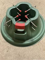 Top-down view showing green metal Christmas tree stand with 6 metal screws with red plastic caps distributed evenly around the holder