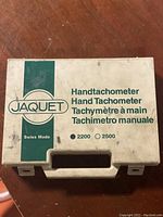 White plastic carrying case with green vertical band and Jaquet logo, labeled Handtachometer in multiple languages and options for 2200 and 2500 RPM.