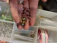 Close-up of hand holding various colored glass and plastic beads including red and yellow ones inside container compartments