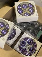 Photo showing multiple boxes of the glass ornaments including shiny purple, matte purple, and black-and-silver varieties.