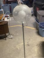 Full side view of the floor lamp standing, showing clear spherical globe shade on top of chrome metal pole and base.
