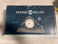Box showing branding and image of ornate mantel clock with decorative scrollwork and Roman numeral clock face
