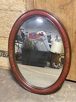 Oval mirror showing hand-painted floral decoration on the reddish-brown frame with reflective glass surface.