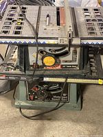 Full view of Ryobi 10-inch table saw on top and Delta 10-inch motorized bench saw below on shelving