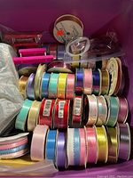 Photo showing over 30 rolls of ribbon in various colors and widths along with two manual ribbon shredders in red and pink.