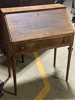 Front view of the small wood secretary desk showing slant front writing surface and drawer with two knobs.