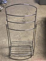 Overall view of silver towel rack showing upper curved frame and lower shelf section