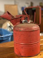 Red vintage oil can showing cylindrical body, hinged spout and handle with visible manufacturer imprint