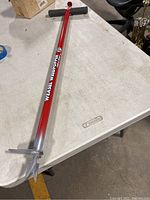 Full image of the Weasel Weedpopper showing the red metal shaft, horizontal handle and metal claw end for weed removal.