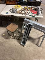 Wide view of table with assorted woodworking tools and small folding stool in front; EBCO metal folding sawhorses on the side
