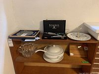 Wooden serving tray with fluted glass bowl, decorative ceramic dish, and other assorted items surfaced on a wooden stand.