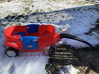Red and blue Little Tikes children's wagon on snow and patio, showing side view with handle and wheels.