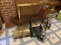 Fireplace screen with brass frame behind fireplace tools and log holders.