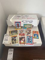 Photo of two white boxes on a table, one smaller box on top with some vintage hockey and baseball cards spread out.
