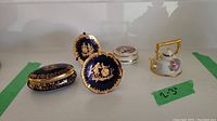 Photo showing group of five Limoges miniatures on display, includes two oval and round trinket boxes, two decorative plates, and a miniature kettle with gold highlights.