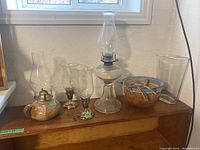 Wide view of entire lot on wooden surface beneath window showing two oil lamps, planter, and vase.