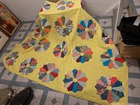Wide view of the full quilt spread over a surface showing the yellow background and multiple circular patchwork blocks.
