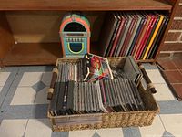 Basket filled with assorted music CDs and nearby Tome Life cookbooks from the 1980s.