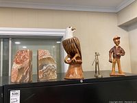 Photo showing the marble bookends, wood carved bird resembling an eagle, abstract metal golfer, and wood carved sailor figurine on top of a black cabinet.