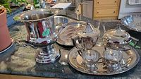 Wide view of silver plated ice bucket urn, tray, tea and coffee pot, cream and sugar on a kitchen counter.