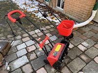 Red and black electric snow shovel on stone patio, showing metal auger and handle